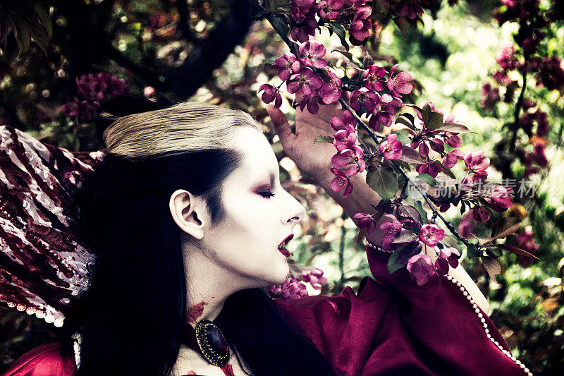 年轻女子在吸血鬼化妆，侧面特写，与深粉红色的春天花朵。