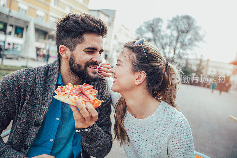 快乐的年轻夫妇在户外吃披萨。