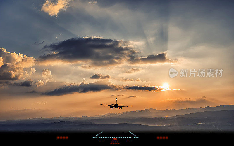 飞机在美丽的夕阳下降落到机场跑道的剪影