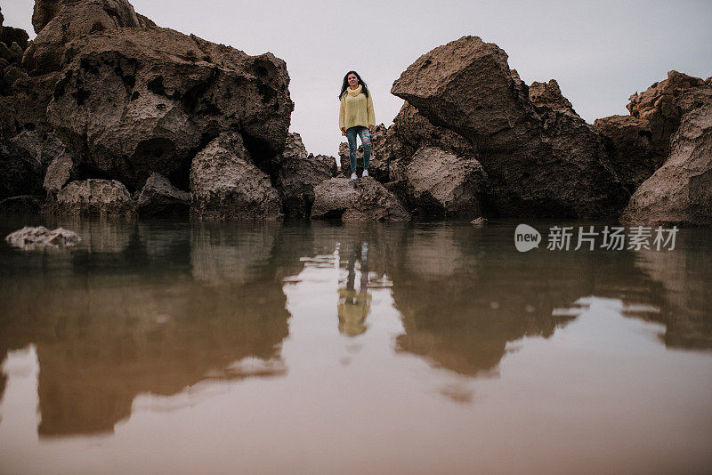 一个年轻女子在海滩的岩石和她在水中的倒影