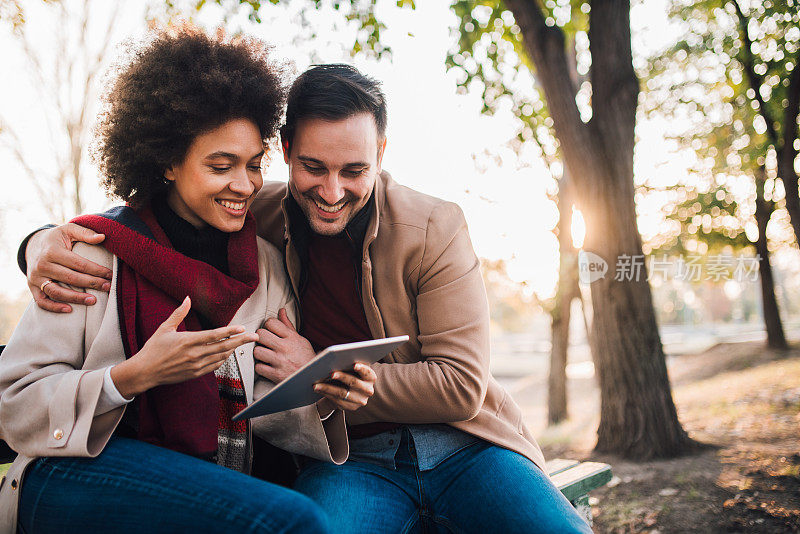 微笑的年轻夫妇在公园的长凳上网上购物