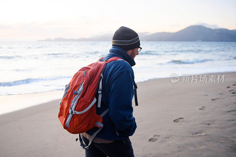 一个背着背包的男人在寒冷的下午行走在旧金山的贝克海滩上