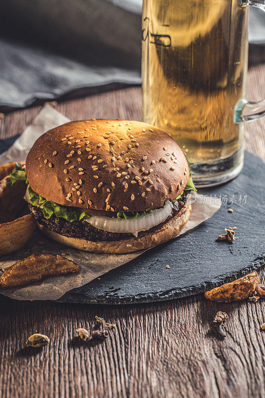 美味的Сheeseburger，一杯啤酒和烤土豆放在木桌上