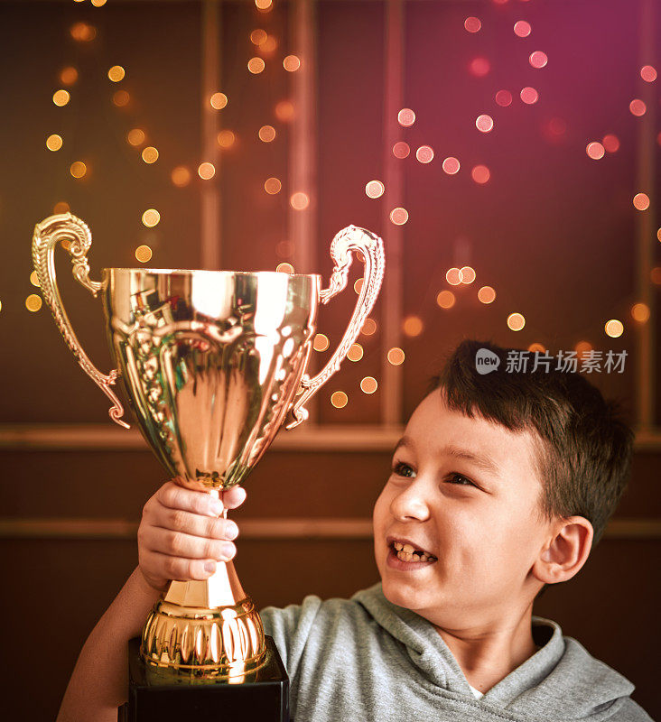 可爱的孩子拿着金杯。他是赢家。