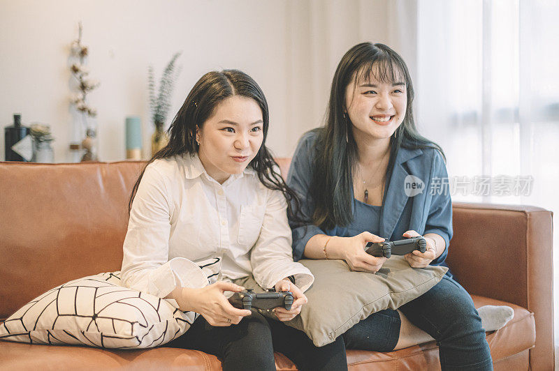 两个亚洲华人女性朋友坐在沙发上玩电子游戏