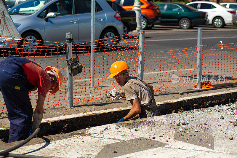 城市街道的维修工作。专业工人用专业工具拆除部分道路。工人们除去沥青并挖一个洞。技术专家，工作流程在城市街道上。