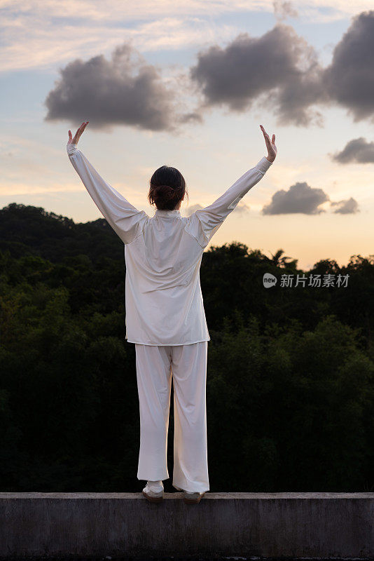 一位亚洲妇女正在公园里练习健身运动太极拳。