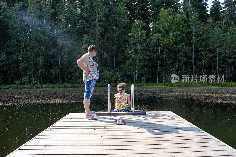 一个77岁的老妇人和一个8岁的白人女孩在森林湖的木码头上。奶奶和孙女在度假。