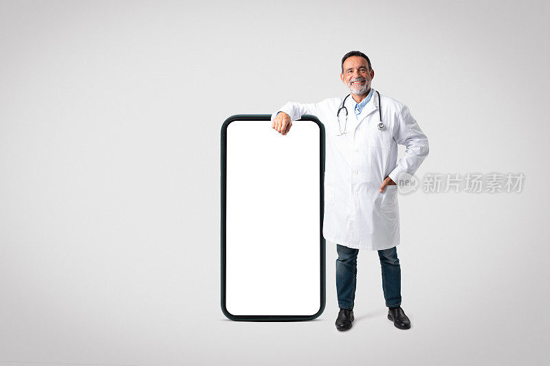 高兴自信的欧洲资深医生穿着白大褂，听诊器靠近大屏手机