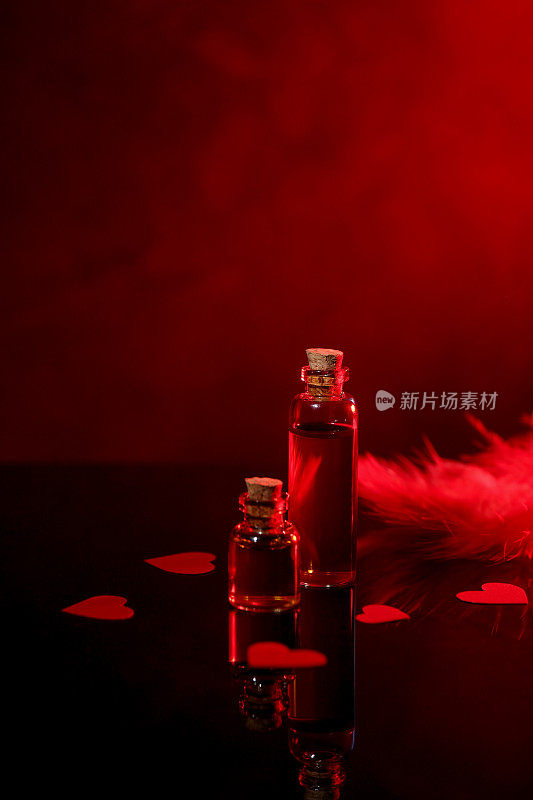 瓶子的爱情药水，纸心和羽毛在镜子表面对黑暗的背景，文字的空间。红色色调效果