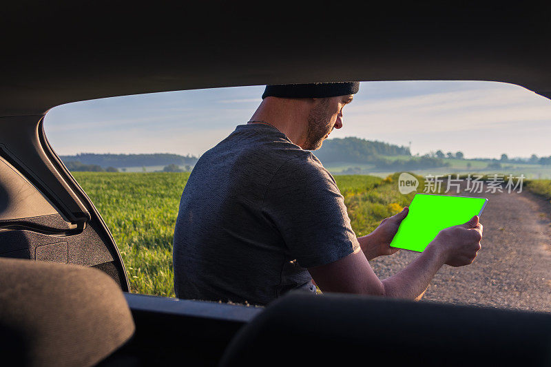 男人，旅行者休息，坐在车里使用绿屏平板电脑。春雾捷克风景
