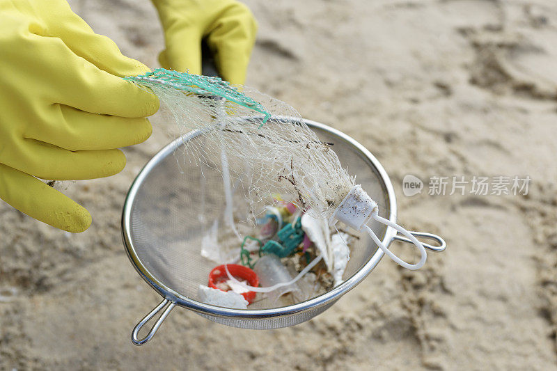一名志愿者戴着手套，用滤嘴清理海滩上的塑料碎片和垃圾。