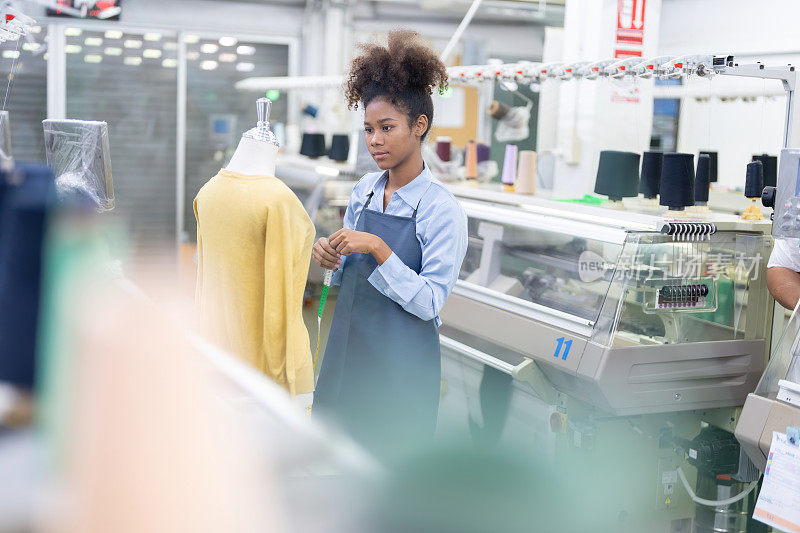广角拍摄的美国女设计师在一家公司的大型制造工厂里，作为裁缝看着服装设计，模特拿着卷尺。