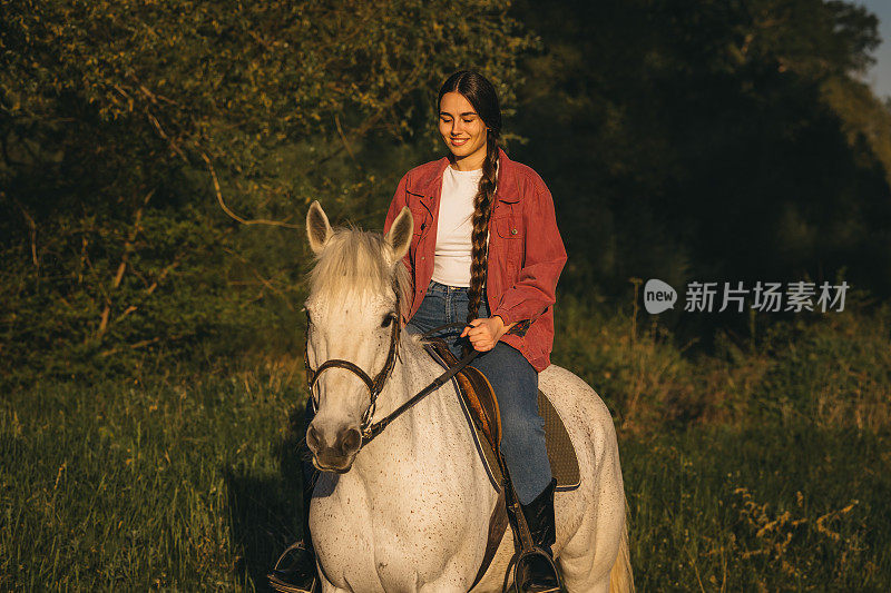 年轻的长发女子在日落时分骑马在大自然中