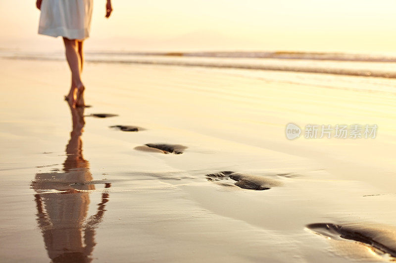 低节女人留下脚印，而行走在潮湿的海滩上