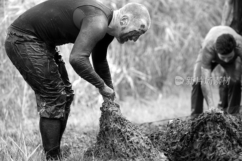 男子帮助在泥跑活动中网障碍
