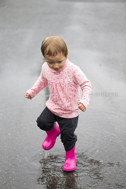 穿着雨靴在水坑里跺脚的小女孩