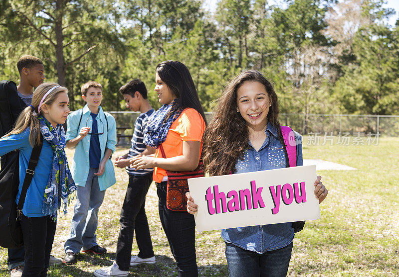 十几岁的拉丁女孩在公园里举着“谢谢”的牌子。