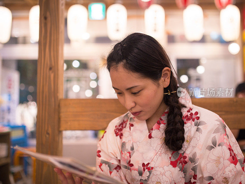 年轻的女子看菜单在日本居酒屋餐厅