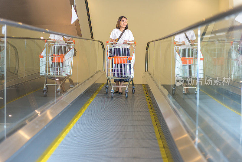 一位女士推着手推车从购物中心的自动扶梯上下来