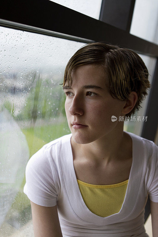 年轻女学生望着窗外的雨