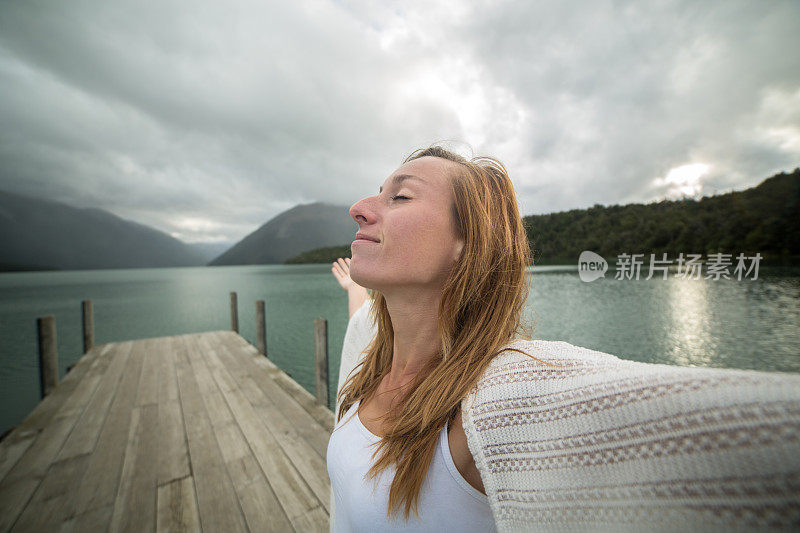 一个年轻女子的肖像在湖码头上张开双臂