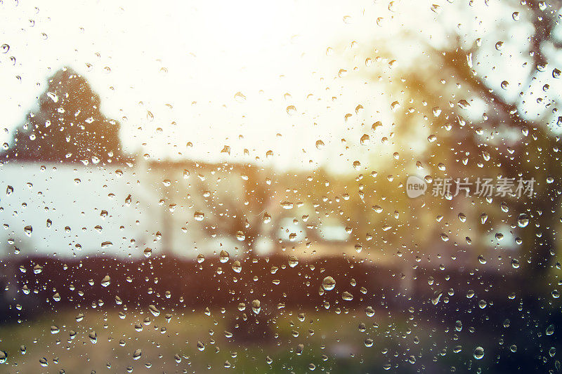 在一个阴雨天，阳光出现在焦点不清的背景下，水珠滴在玻璃窗户上的特写画面