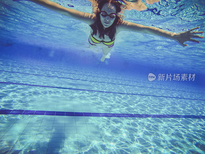 年轻的女游泳运动员戴着泳镜在游泳池里游泳