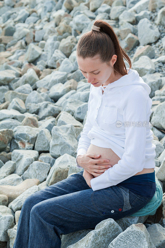 悲伤的孕妇独自坐在石头海滩上