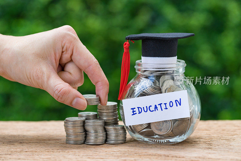 女人手里拿着一叠硬币和装满硬币的玻璃罐子和毕业生帽子，标签上写着教育、教育或储蓄的概念