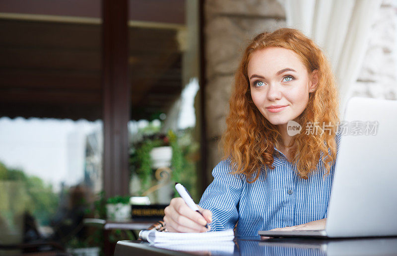 年轻的红发女孩在笔记本上做笔记