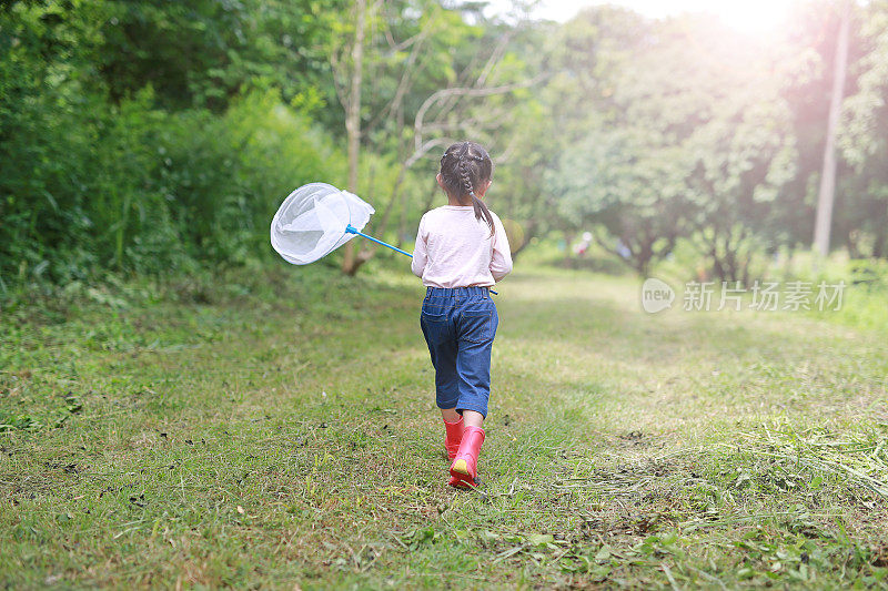 亚洲小女孩在夏天的田野里玩捕虫网，后视图。