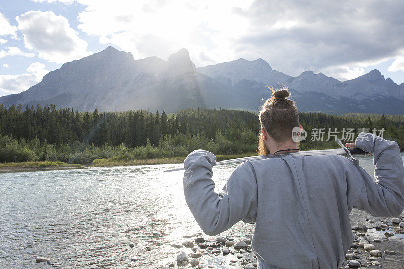 一个穿着诺曼服装的年轻人站在河边，望着群山