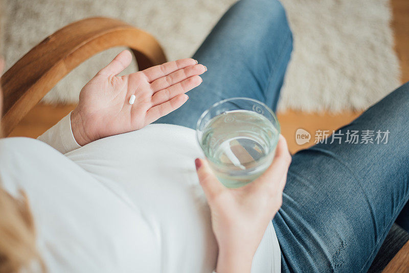 孕妇拿着一粒药丸和一杯水