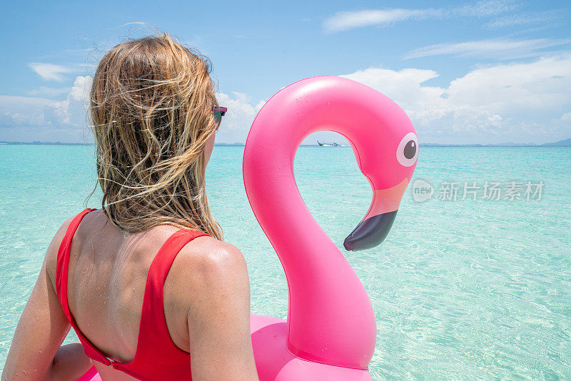 年轻女子放松在田园诗般的海滩充气火烈鸟玩在纯净的水在泰国岛屿。人们旅行奢侈，乐趣和酷的态度概念