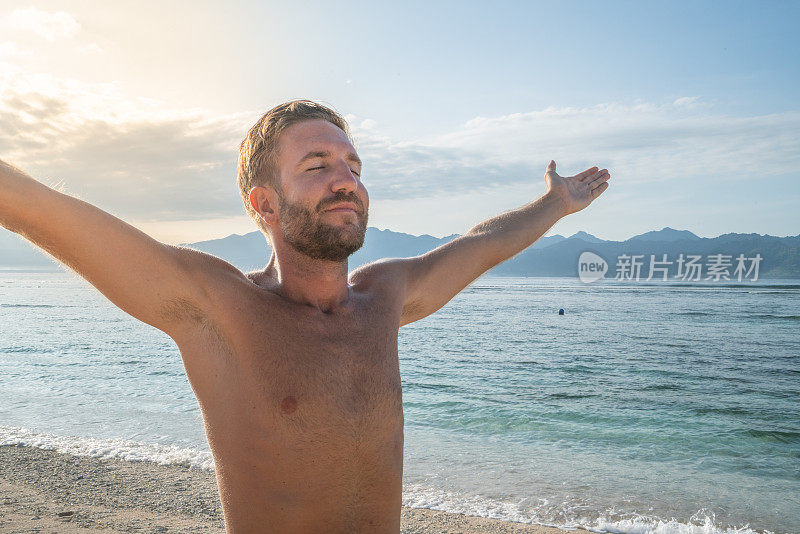 年轻人在海滩上伸开双臂享受热带气候和异国情调的假期。旅游目的地自由的人好奇的概念自然