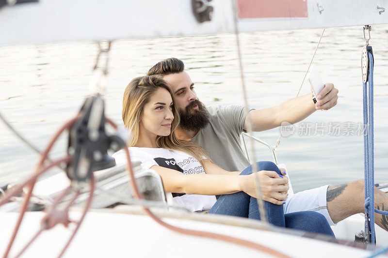 一对迷人的情侣在一艘帆船上放松、拍照和使用智能手机