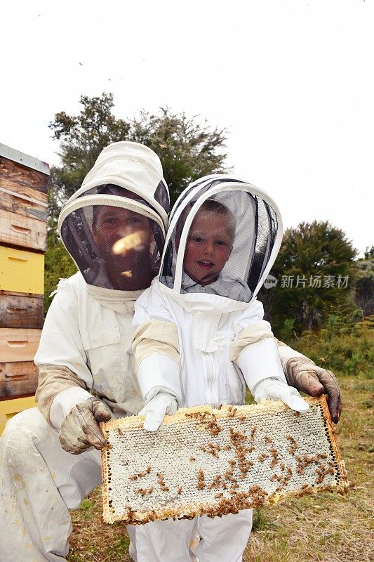 孩子在蜜蜂套装拿蜂蜜框架与导师