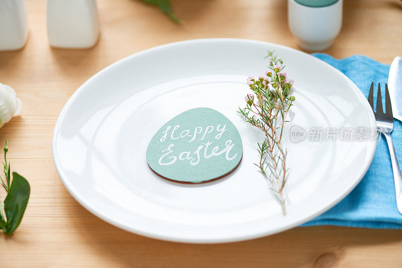 木桌上摆放着白色陶瓷盘子，上面有可爱的小花和复活节彩蛋卡片