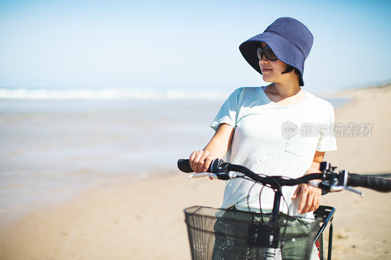 年轻的成年女子骑着自行车在海滩上