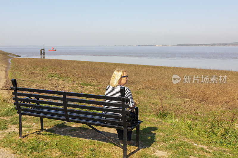 一位年长的女士坐在长凳上望着亨伯河，陷入了沉思。