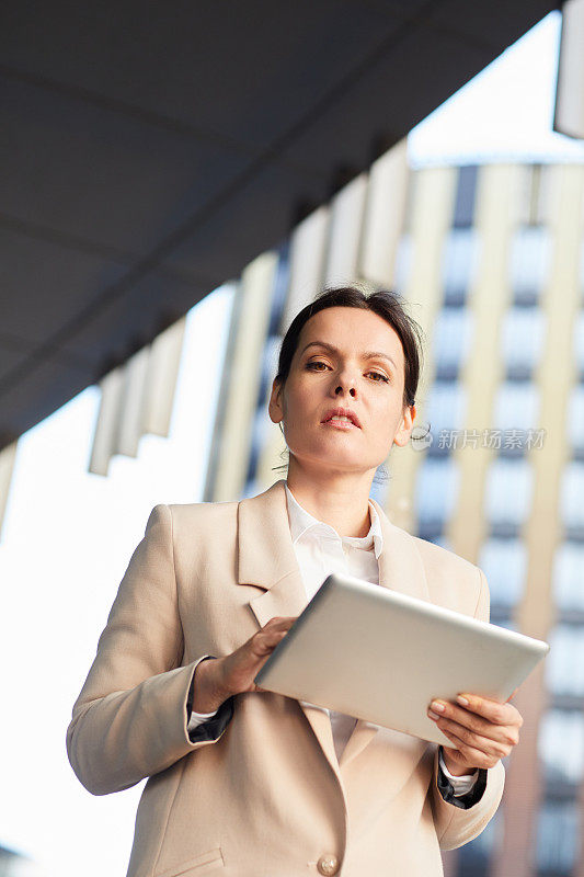 下图是一位棕色头发的严肃严肃的女性商业分析师，她一边走在街上一边用平板电脑工作