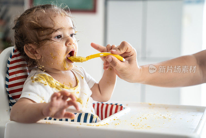 女婴坐在喂食椅上吃婴儿食品