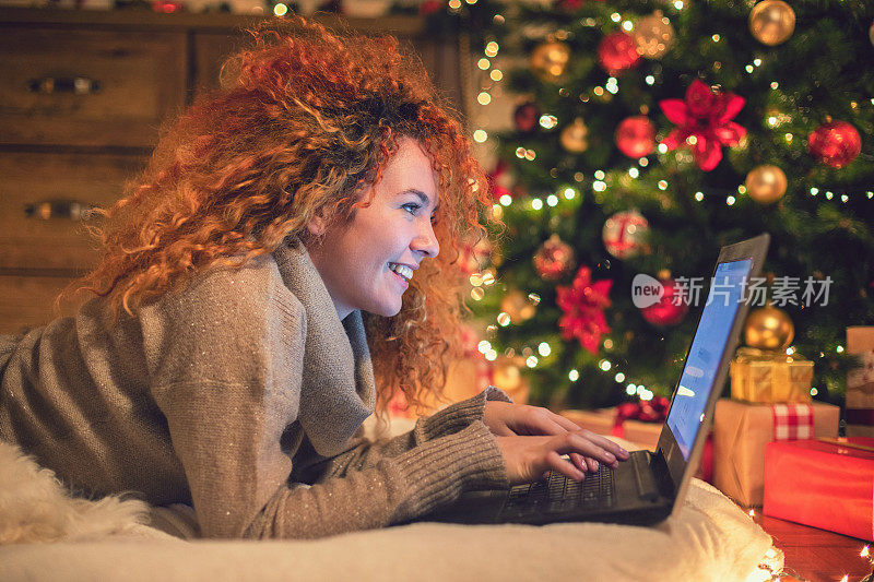 年轻美丽的女孩享受在家里使用笔记本电脑在一个舒适的圣诞气氛