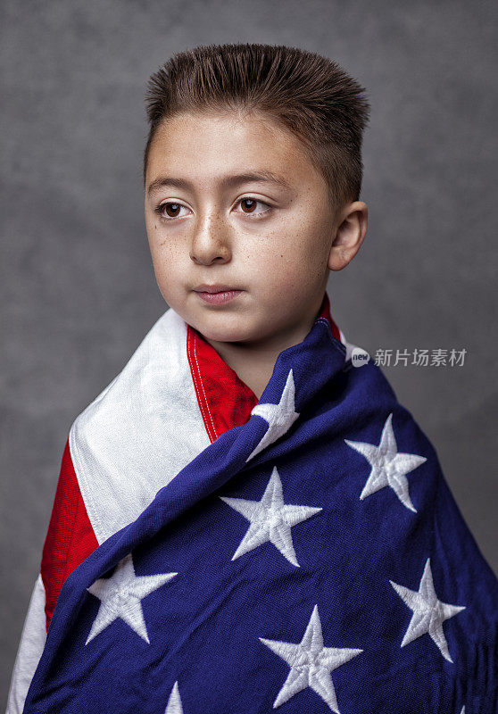 亚裔白人混血小男孩，浅黑色平顶发型，裹着美国国旗，在灰色的背景下摆姿势