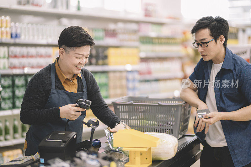 一位亚洲华裔女售货员收银员在收银台使用条形码扫描仪扫描顾客的物品