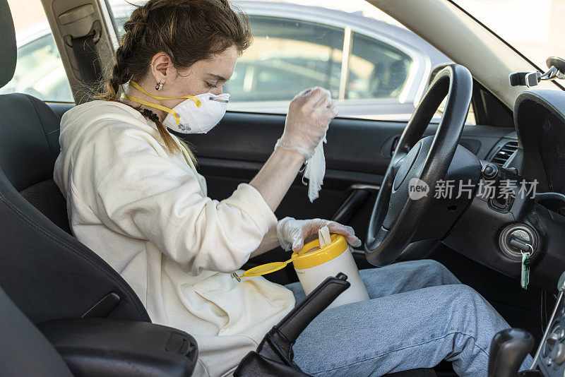 一名年轻女子戴上防护口罩，坐在车内用消毒湿纸巾清洁双手，从容器中取出消毒湿纸巾