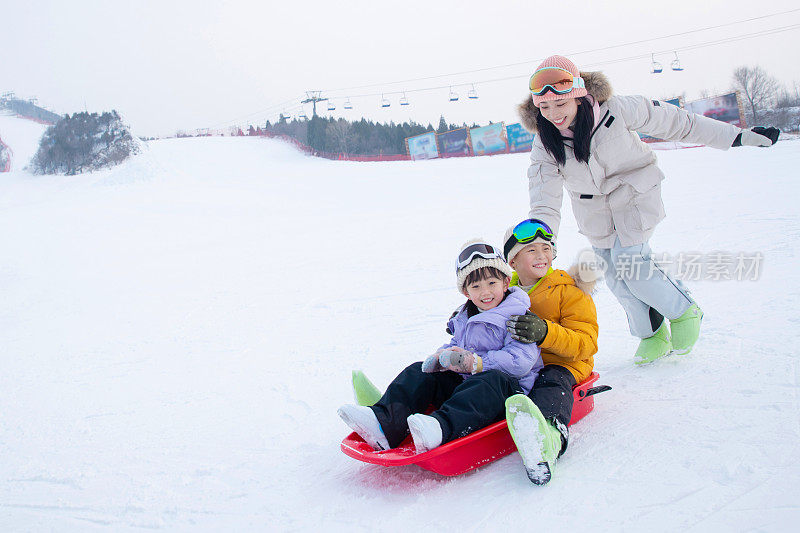 滑雪场上妈妈推着坐在雪上滑板的孩子们