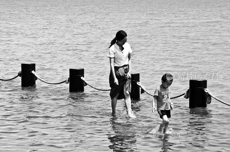 一名中国母亲和孩子在深圳人才园附近的湖中享受清凉的黑白图像。这个公共主题公园与深圳湾公园和湾体育馆相连