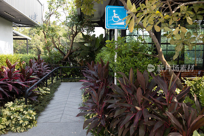 大楼前的残疾人指示牌。残疾人标志交通标志在坡道前地板上支持轮椅。在绿色自然景观的咖啡馆前的残疾人道路标志。